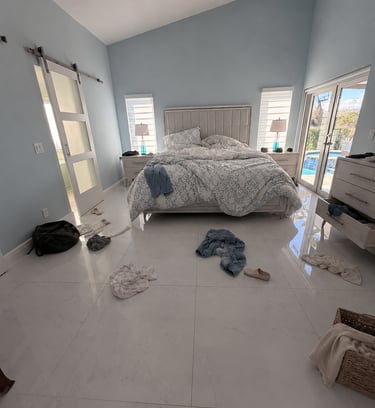 Messy modern master bedroom with clothes on marble tile flooring and light blue walls.