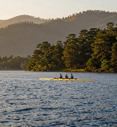 Wide-angle panoramic view of Naini Lake surrounded by misty pine hills at golden hour, a single classic rowing boat on the water, warm editorial travel photography style