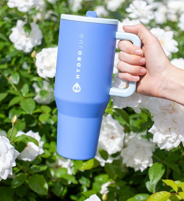 a person holding a blue coffee mug in front of a bush