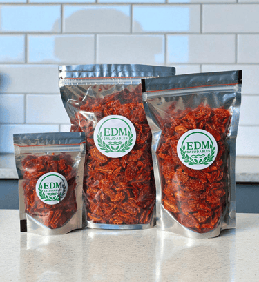 Tres tamaños de envases con tomates cherry deshidratados, sobre mesada de mármol.