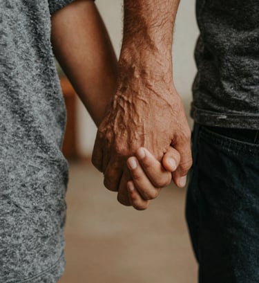 A close-up artistic shot of a parent's hand holding a child's hand in a South American / Brazilian home setting. Warm light grey and dark charcoal tones in the clothing. Soft focus background, intimate and emotional atmosphere.