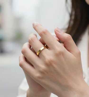 A close-up shot of two hands intertwined, featuring a minimalist gold ring. Soft focus on a clean white background in a North American / US urban setting. Elegant and refined.