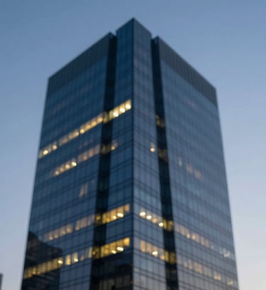 Abstract architectural photograph showing the sharp corner of a modern skyscraper against a twilight sky. Strong geometric lines in dark blue steel and glowing yellow windows. Clean, professional, and forward-thinking aesthetic.