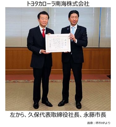 堺市役所の応接室で、トヨタカローラ南海株式会社の久保尚平代表取締役社長(左)と永藤英機堺市長(右)が、ガス気球を活用した堺観光活性化事業への100万円の寄付に伴い、感謝状を手に並んで立つ様子|堺市のニュースならサカイタイムズ