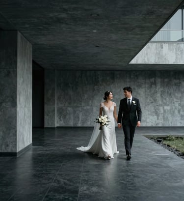Cinematic wide shot of a bride and groom walking through a minimalist modern architectural space in a South American / Colombian city. Dark charcoal and soft silver tones.