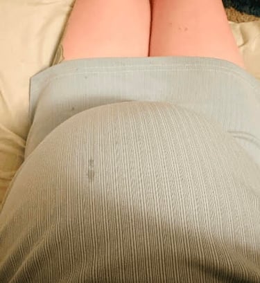 Mother looking down on her 9 month pregnant belly wearing a blue dress with a teardrop.