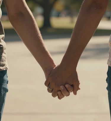 A close-up candid shot of two people sharing an authentic, heartfelt moment, holding hands in a sun-drenched North American / General Western park. Shallow depth of field with warm cinematic lighting and natural charcoal and soft sand colors in the environment.