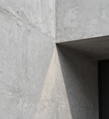 Close-up photography of a polished concrete wall in a Brazilian design studio. A single ray of light hits the surface, revealing smooth texture. Sophisticated and minimalist composition, neutral light grey and black tones.