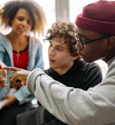 Diverse students collaborating and looking at a smartphone screen together in a classroom.