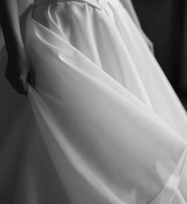 An artistic black and white style photograph using dark charcoal and soft off-white tones. It depicts a candid, blurry movement of a wedding dress fabric, evoking a sense of calm and sophisticated movement. Professional and high-end.