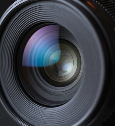 A macro shot of a camera lens element, reflecting neon blue and muted slate light patterns, extremely sharp detail, dark slate shadows.
