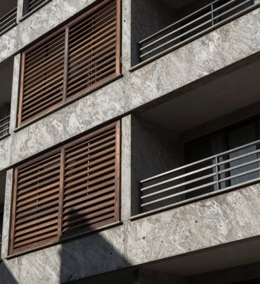 A close-up, high-contrast architectural detail shot of a modern residential facade in a South American / Brazilian urban environment. Focus on the interplay between dark wood louvers and raw gray concrete. Sharp, direct sunlight creating a rhythmic shadow pattern.