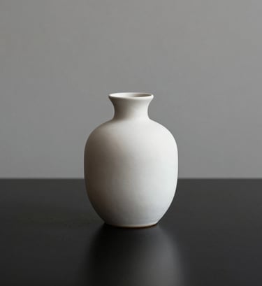 An artistic, minimalist still life of a single off-white (#F8F8F8) ceramic vase on a black surface (#000000). The composition is clean and centered, with soft lighting from the side creating a gentle gradient. Reflects a modern and refined brand identity.