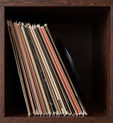 An artistic shot of vintage vinyl records stacked vertically in a dark cocoa brown wooden shelf. The edges of the records catch a muted terracotta light, creating a sophisticated and warm artistic atmosphere.