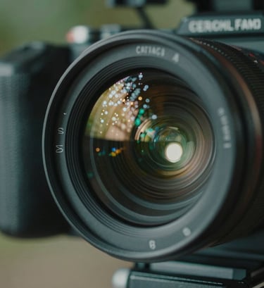 A close-up, artistic shot of a professional film camera lens reflecting the lights of a South American / Brazilian film set. The color palette features deep sea green shadows and sharp pearl white highlights, conveying a sense of high-end cinematic production.