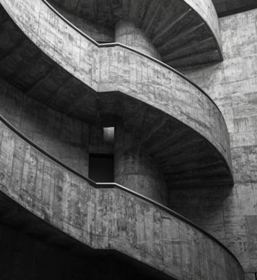 A stark black and white style architectural photograph of a concrete spiral staircase. The image uses tones of dark charcoal and soft sage highlights to emphasize the texture and professional craftsmanship of the brutalist structure.