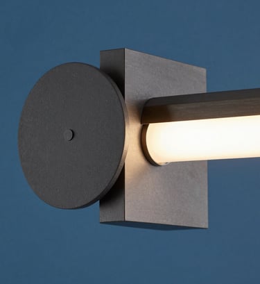 A sharp, close-up photograph of a geometric light fixture designed with Bauhaus aesthetics. The lamp features clean circular and square components in dark gray and brushed steel, set against a cerulean blue backdrop in a sophisticated North American interior.