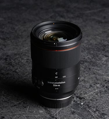 Commercial product photography of a high-end luxury camera lens on a dark gray marble surface, dramatic side lighting with deep blacks and sharp reflections, International / Professional aesthetic.