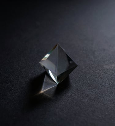 A moody, artistic photograph of soft light passing through a glass prism, casting faint indigo shadows across a dark charcoal surface. The style is abstract and cinematic, reflecting a thoughtful and creative North American / US design aesthetic.