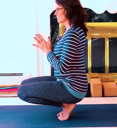 A woman 50+ balances in a yoga pose on tip-toe seated on her heels. hands in prayer