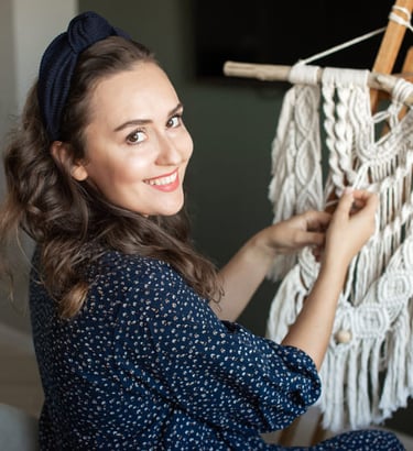 Mujer de espaldas, sonriendo mientras teje macrame blanco