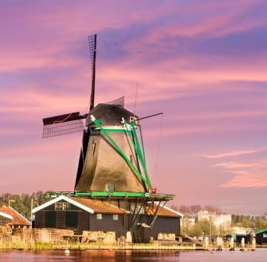 Traditional Dutch windmill at Zaanse Schans against a pink sunset sky by the water.
