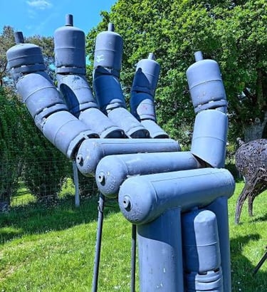 A large metal hand sculpture made of blue recycled gas cylinders standing in a green garden.