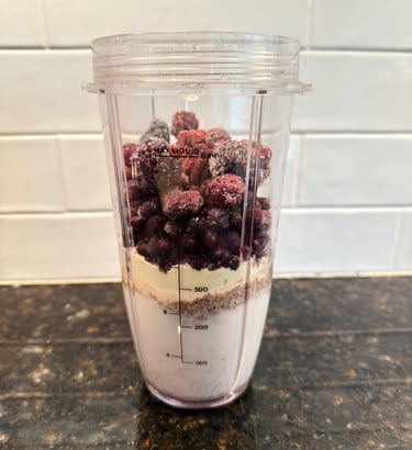 Protein smoothie ingredients layered in a blender cup with berries and almond milk.