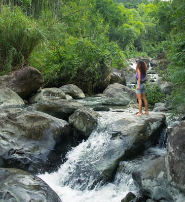 Woman standing on rock as she looks ahead, by a mountain cascade in Pu Luong Vietnam