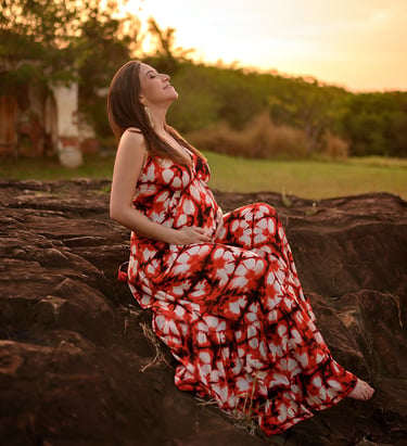 Mulher de vestido vermelho longo sentada em meio a natureza com paisagem