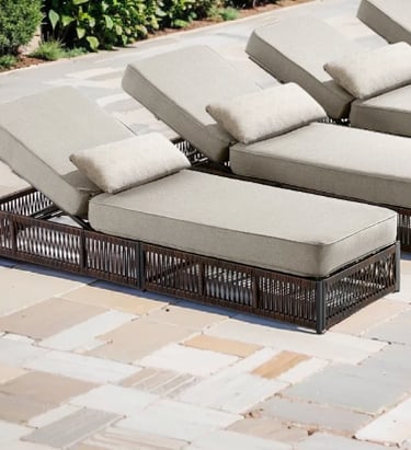 Wicker outdoor lounge chairs with beige cushions on a stone patio poolside.