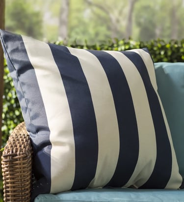 Navy blue and white striped outdoor decorative pillow on a wicker patio chair with teal cushions.