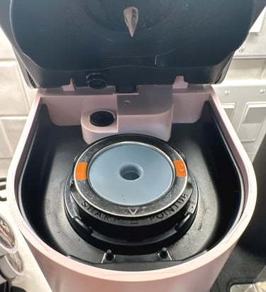 Inside view of a pink Keurig coffee maker pod holder with sharp needle and filter assembly.