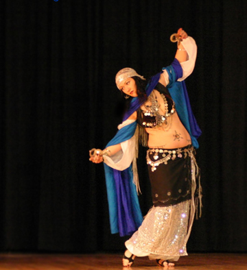 Shahravar Arabic style dancer wearing coin bedlah playing finger cymbals while wearing a white spark