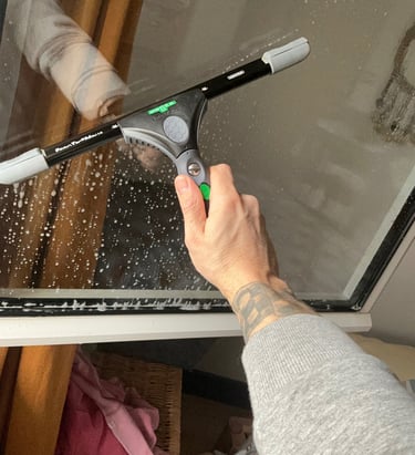 Main nettoyant une vitre avec une raclette
