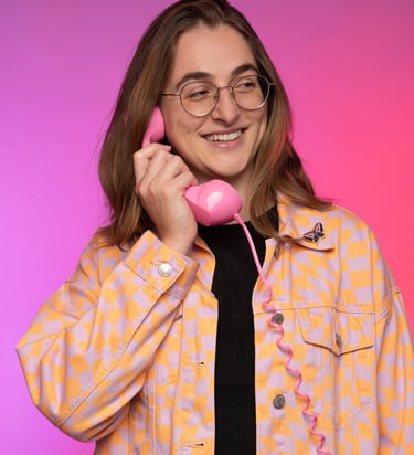 a woman in a purple and orange jacket holding a pink phone up to her ear and smiling