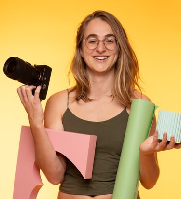 a woman holding a camera and product photography props such as a paper roll and blocks