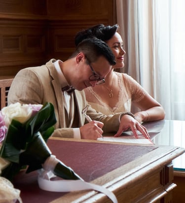 Couple de mariés signant leur acte de mariage et un bouquet de fleurs au premier plan.