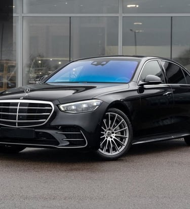 Luxurious black Mercedes-Benz S-Class sedan parked outside a modern car dealership showroom.