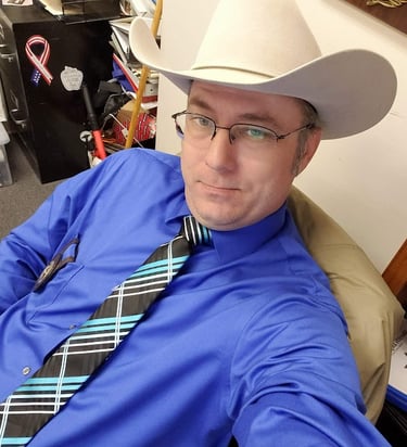 The Author, Steven L Riddles Jr, blue shirt, blue and black tie, with a grey cowboy hat.