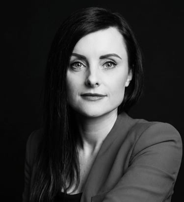 Professional black and white corporate headshot of a brunette woman against a dark background.