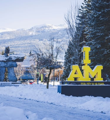 A yellow "I AM" Invictus Games sign in front of a snow-covered Whistler village