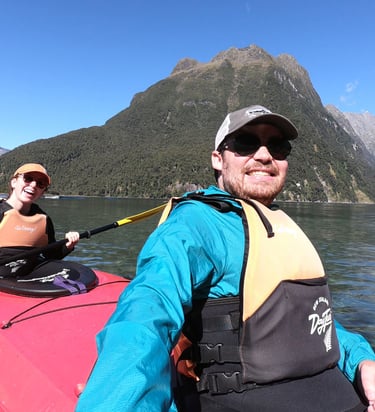 Sean wearing a teal jacket and ball cap in a kayak in New Zealand's Milford Sound
