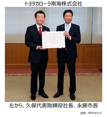 堺市役所の応接室で、トヨタカローラ南海株式会社の久保尚平代表取締役社長(左)と永藤英機堺市長(右)が、ガス気球を活用した堺観光活性化事業への100万円の寄付に伴い、感謝状を手に並んで立つ様子|堺市のニュースならサカイタイムズ