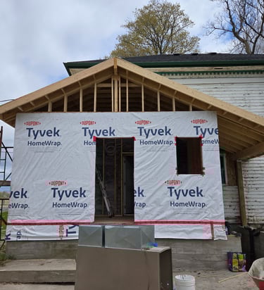 A house addition under construction with Tyvek HomeWrap weather barrier and a new wooden roof frame.