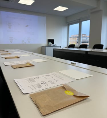Hand lettering workshop materials including instructional sheets and brown paper bags on white tables in a classroom.