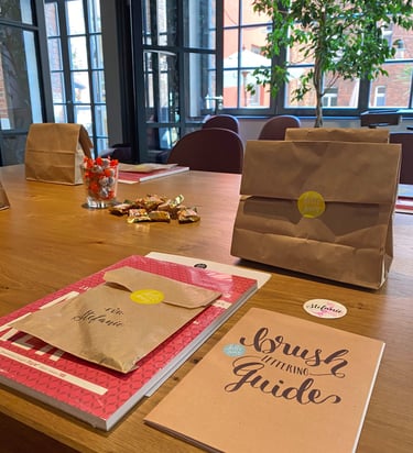 Brush lettering guide and brown paper gift bags on a wooden table at a creative workshop.