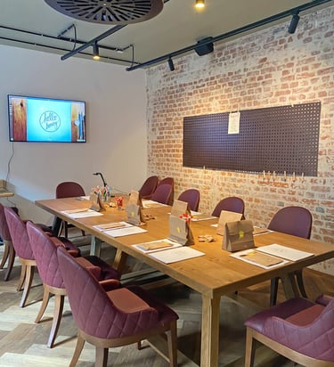 A rustic meeting room with a wooden table, burgundy chairs, and an exposed brick wall.