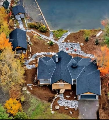 Aerial view of a luxury lakeside cottage with stone walkways and autumn foliage.