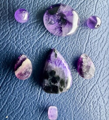 Amatista y charoíta pulidas en diferentes formas sobre una superficie azul texturizada.